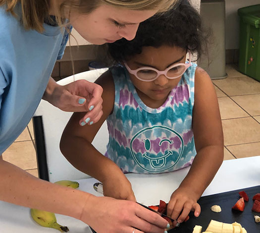Woman helping a young girl cut bananas and strawberries